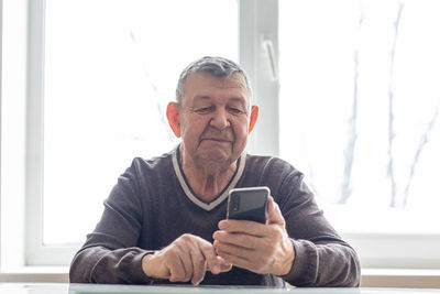 Elderly man dials number in smartphone from home. old senior sends sms on mobile phone