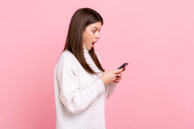 Young woman using mobile phone against pink background