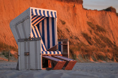 Hooded chairs on beach against sky during sunset