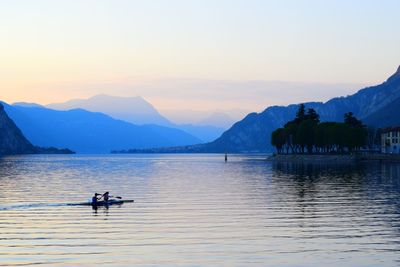 People rowing boat on lake against sky during sunset