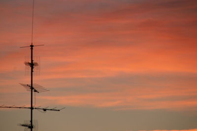 Low angle view of power lines against orange sky