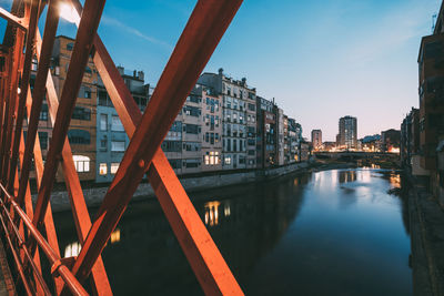 Bridge over river by buildings against sky