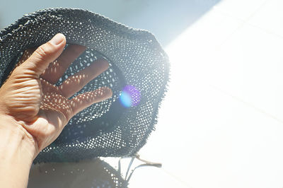 Cropped hand holding hat on retaining wall during sunny day