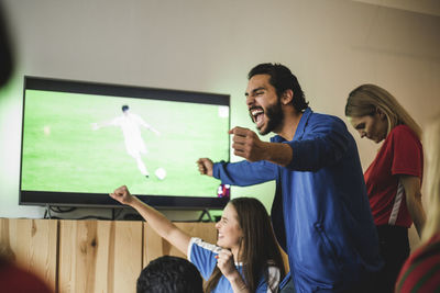 Cheerful man celebrating goal while standing with friends at home