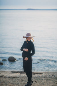 Beautiful young pregnant woman in a black turtleneck and black tight skirt, a classic beige hat 