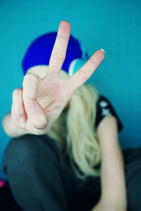Close-up of woman gesturing peace sign against blue wall