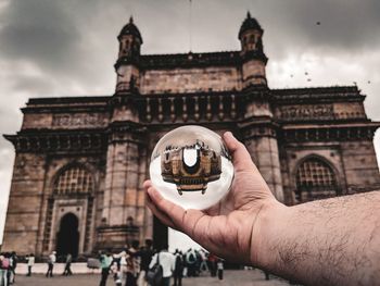 Cropped hand holding crystal ball with gateway of india reflection