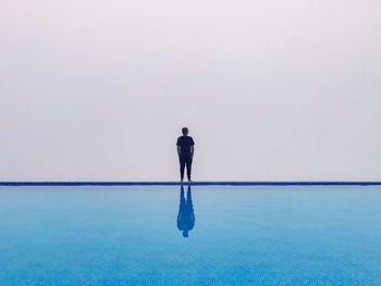 Rear view of standing by infinity pool against sky