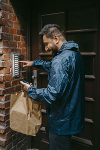 Smiling male food delivery person ringing doorbell while standing outside house