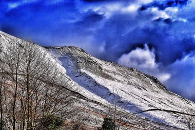 Low angle view of snow covered mountains against cloudy sky