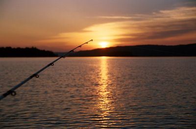 Close-up of fishing rod over lake against sky during sunset