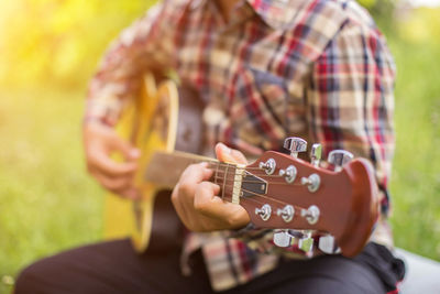 Midsection of man playing guitar in park