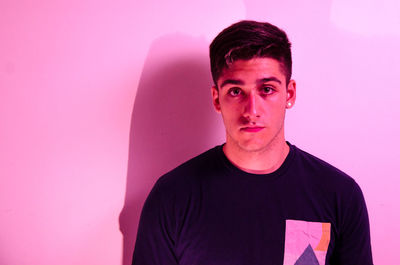Portrait of young man standing against pink background