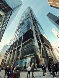 People walking on street amidst modern buildings in city against sky