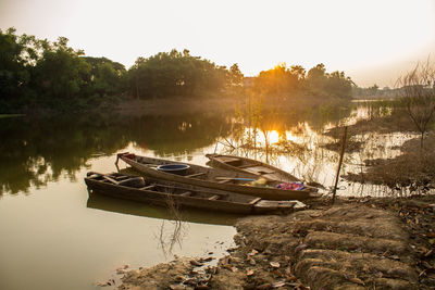 Boat moored in lake against sky during sunset