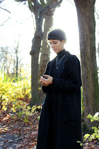 Young woman in coat using phone while standing on field