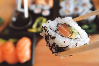 Close-up of chopsticks holding sushi roll over table