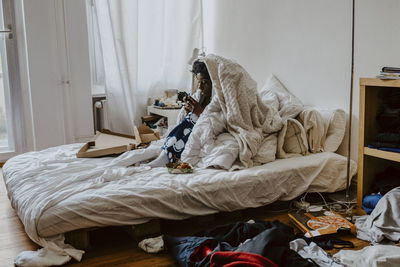 Woman text messaging on smart phone while sitting in bedroom