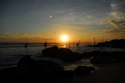 Silhouette fisherman on stilt at sea against sky during sunset