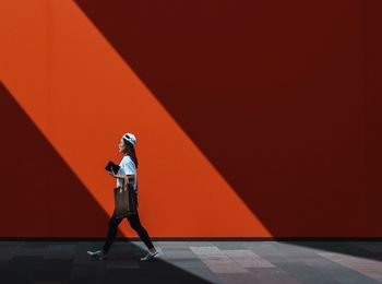 Side view of woman standing against red wall