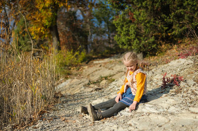 Girl playing. preschooler child sits on the ground on a clear sunny autumn day in the forest