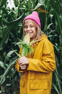 Stylish teenage girl in yellow raincoat and hot pink hat laughing on corn field