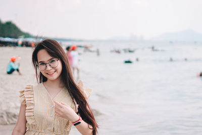 Portrait of beautiful woman wearing sunglasses gesturing while standing at beach