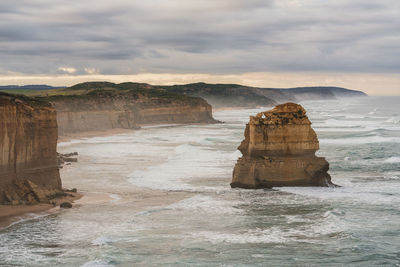 Moody scenery along great ocean road with rock formation on sea shore against sky