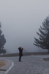 Full length of woman photographing while standing on road during foggy weather