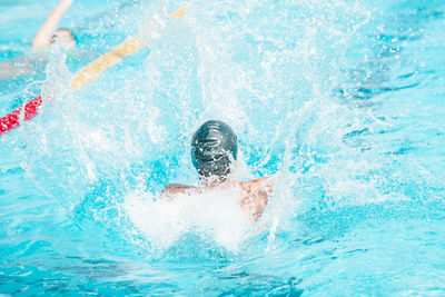 Rear view of man splashing water in swimming pool