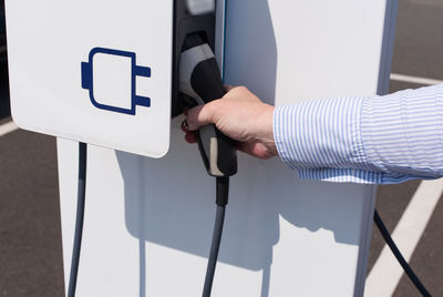 Cropped hand holding charger at electric vehicle charging station