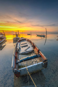 Fishing boats moored on sea against sky during sunset