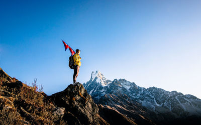 Man holding nepali flag while standing on mountain against clear blue sky