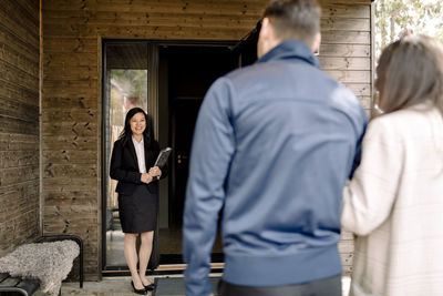 Smiling real estate agent greeting couple at entrance of house