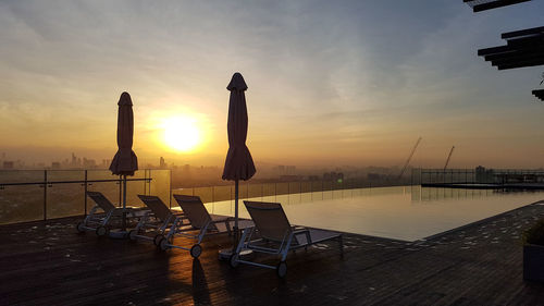 Chairs by swimming pool at beach against sky during sunset