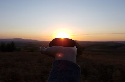 Person hand on field against sky during sunset
