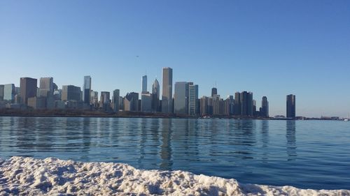 Modern buildings by sea against clear sky