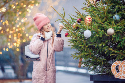 Portrait of young woman standing by christmas tree