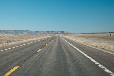 Road by landscape against clear blue sky