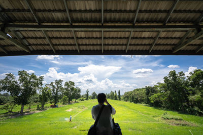 Rear view of woman sitting on landscape against sky