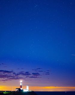 Illuminated lighthouse against blue sky at night