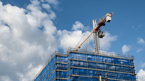 Low angle view of crane at construction site against sky