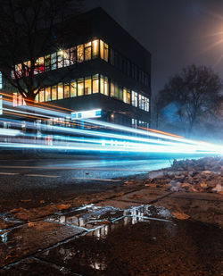 Light trails on street by buildings against sky at night