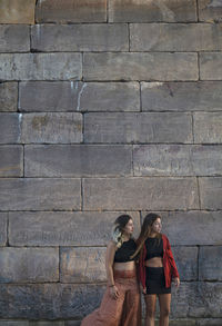 Portrait of two girls standing against stone wall