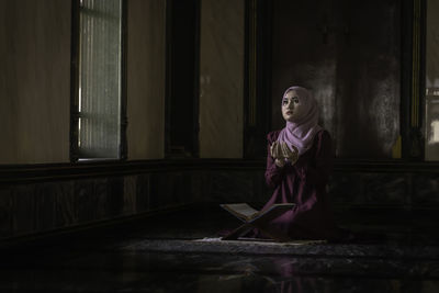 Woman looking away while sitting on window