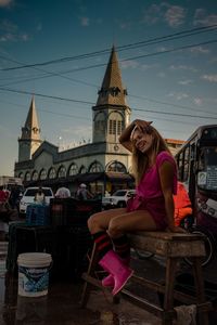 Woman sitting on chair outside building against sky