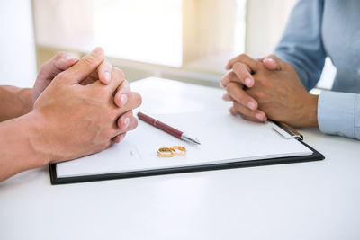 Midsection of couple sitting with divorce paper and rings on desk in courtroom