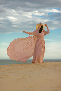 Rear view of woman standing at beach against sky