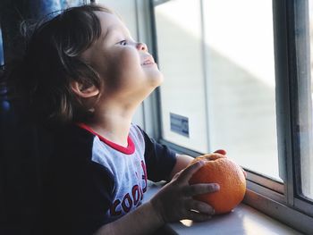 Cute boy holding orange by window at home