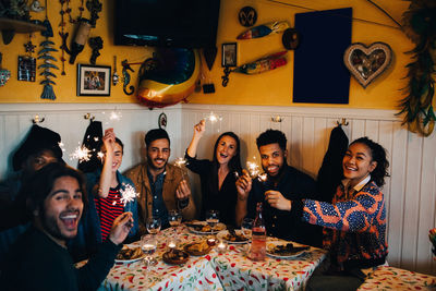 Portrait of cheerful young multi-ethnic friends sitting with sparklers at table in restaurant